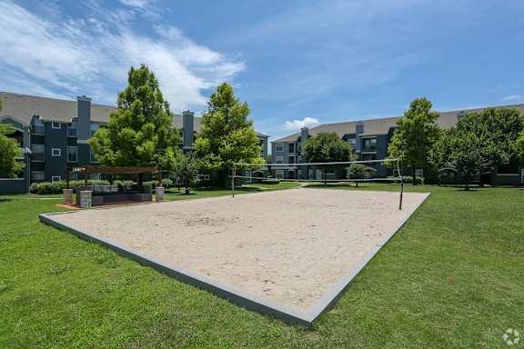 A sand volleyball court is surrounded by grass and trees.