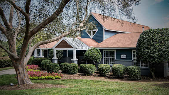 A blue house with a white trim and a large tree in front.