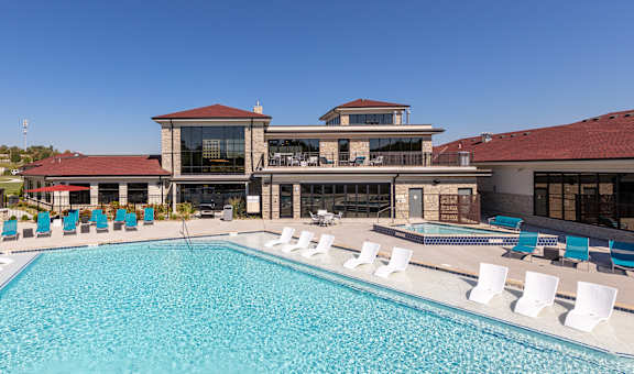 A large swimming pool with white lounge chairs and a multi-story building in the background. at Trinity Woods Apartments, Independence, 64015