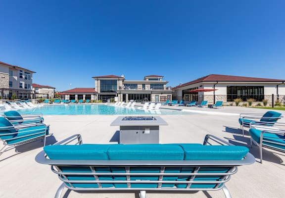 A sunny day at the pool with blue lounge chairs and a building in the background. at Trinity Woods Apartments, Independence, 64015