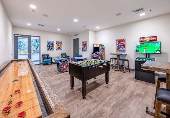 A room with a pool table, arcade games, and a TV. at Trinity Woods Apartments, Independence, 64015