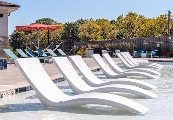 A row of white lounge chairs are arranged in a pool. at Trinity Woods Apartments, Independence, 64015