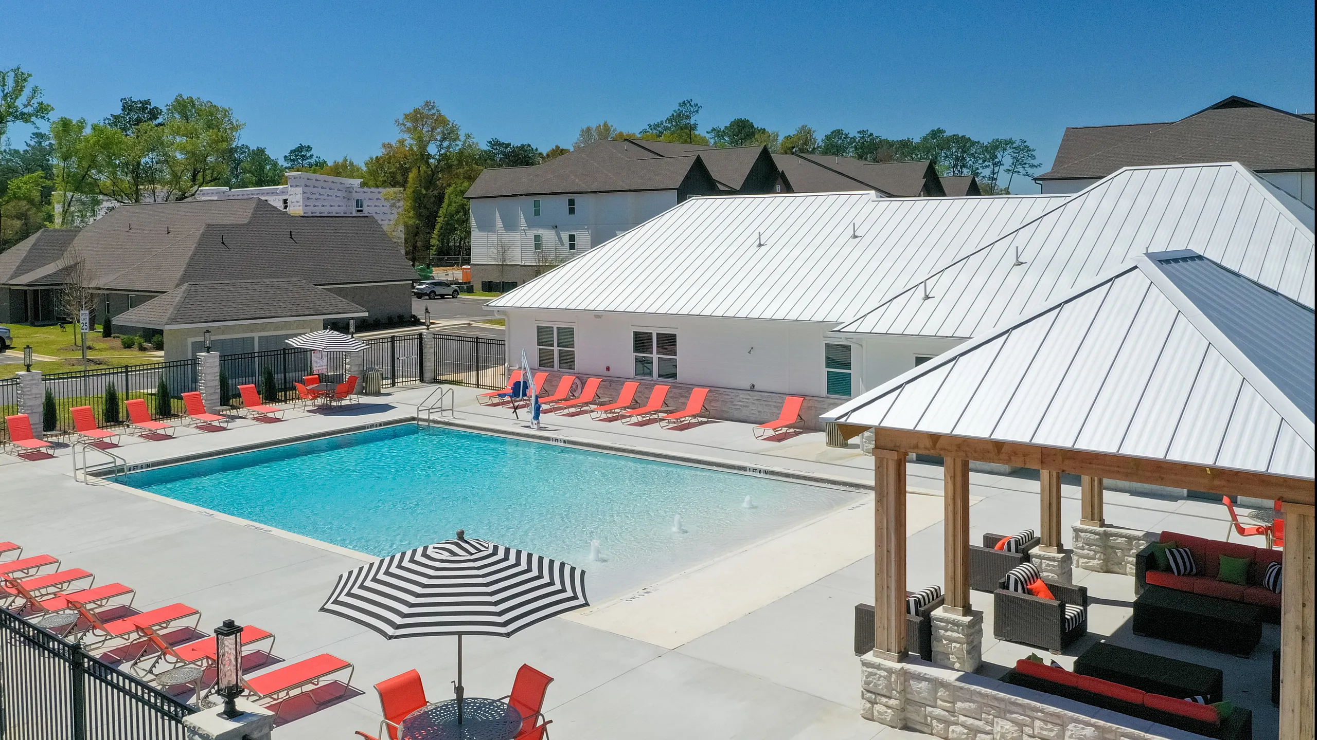 Inviting apartment complex with a sparkling swimming pool, vibrant red lounge chairs, and stylish cabana seating under clear blue skies.