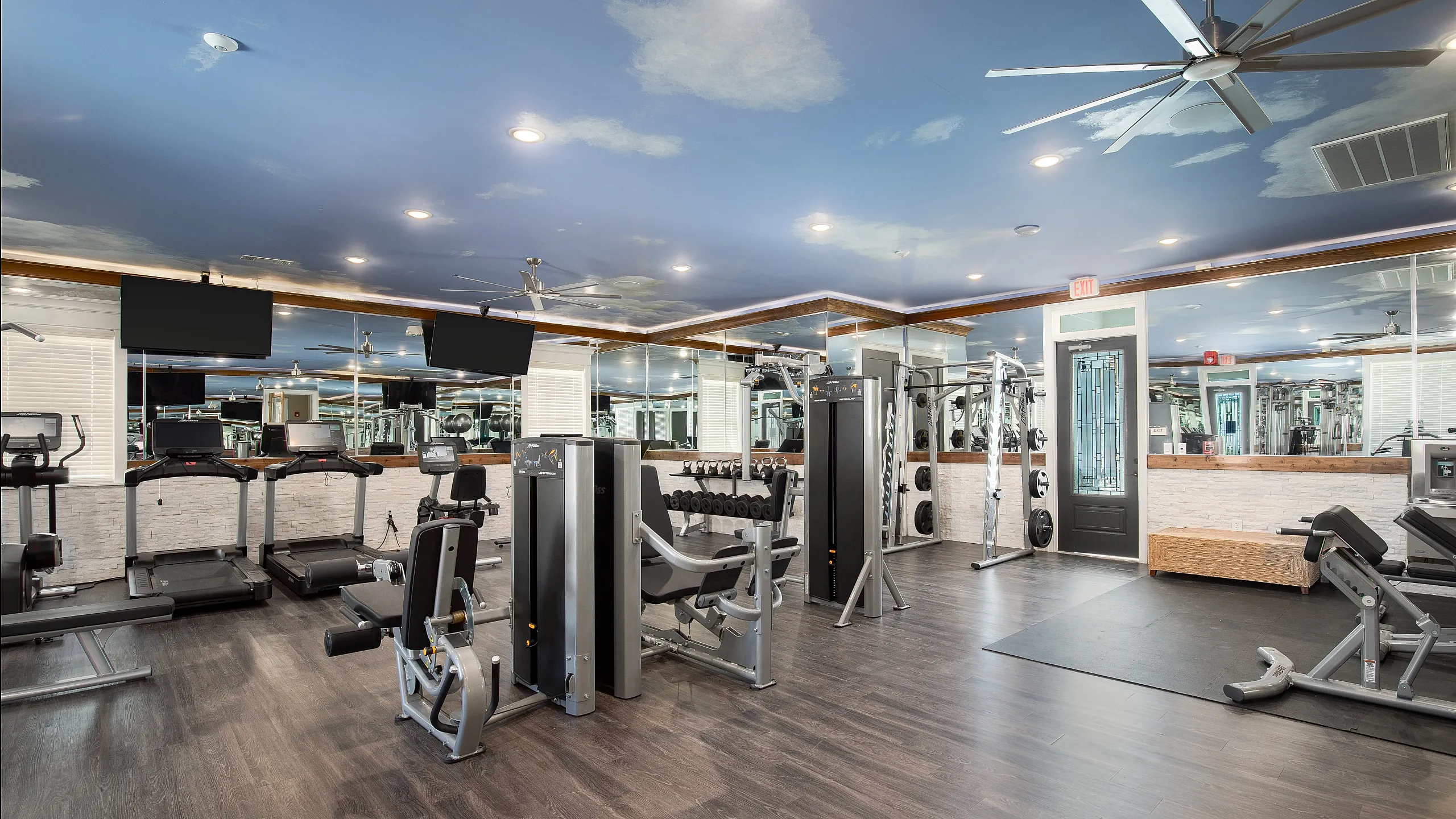 Luxurious apartment gym featuring modern fitness equipment, stylish wood flooring, and a serene sky-themed ceiling design.