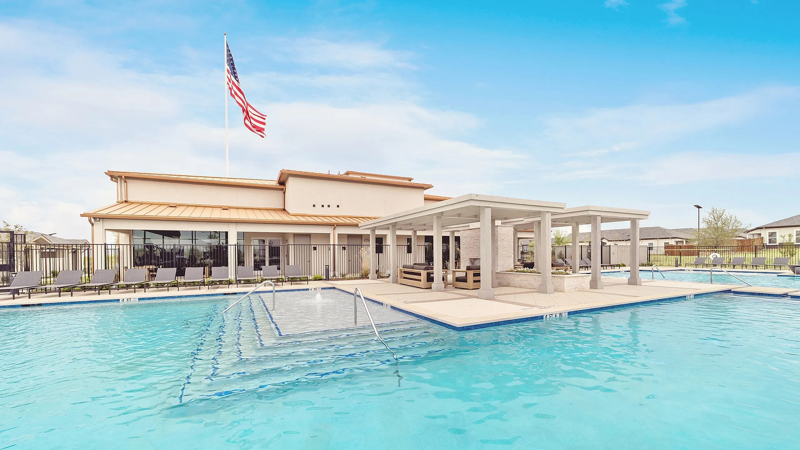 Luxurious apartment complex with a sparkling outdoor pool, stylish lounge area, and modern architecture under a vibrant blue sky.