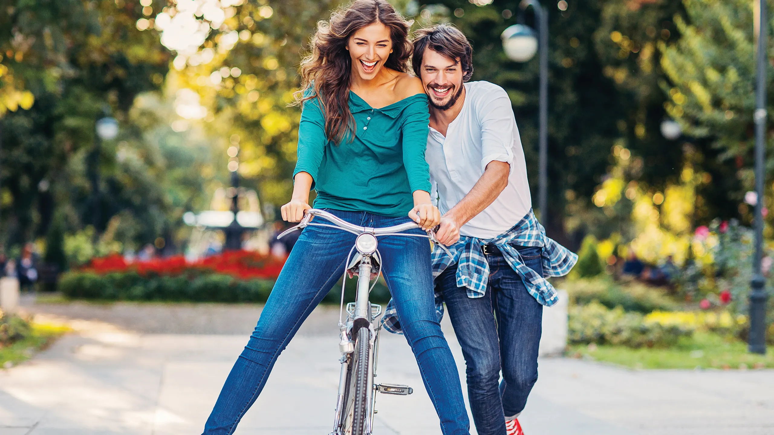 Joyful couple riding a bicycle in a sunlit park, embracing fun and freedom.