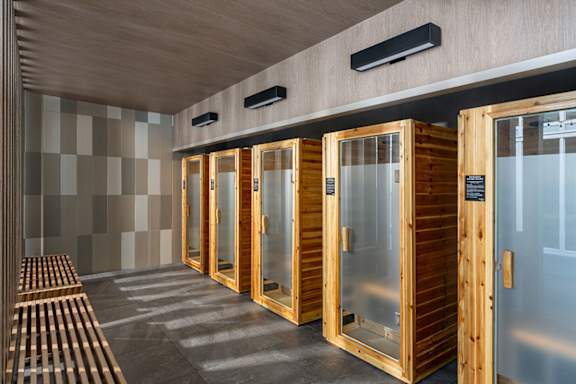 A row of wooden saunas with glass doors are lined up in a room.