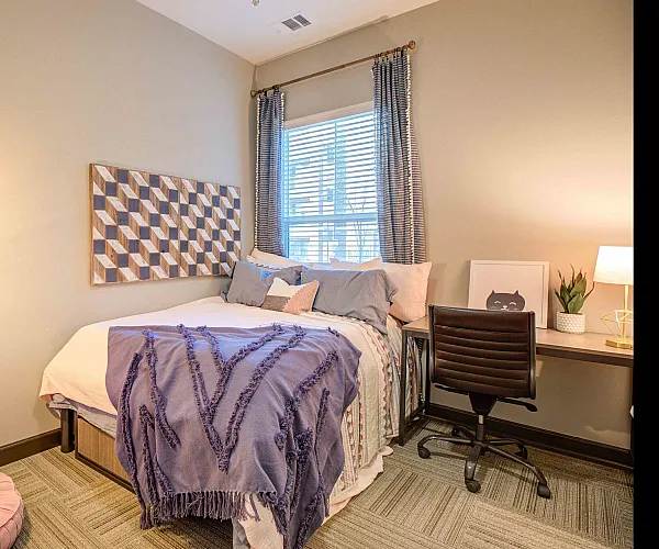 Model apartment bedroom with a full size bed, desk, and desk chair