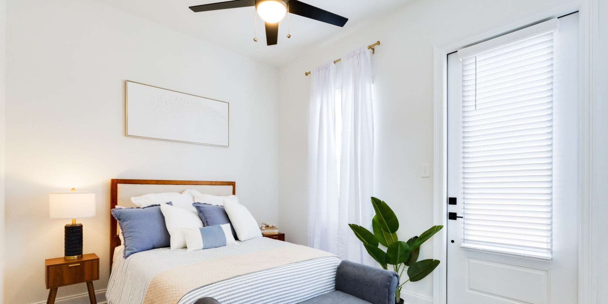 Bright bedroom with ceiling fan, light curtains, decorative plant, and cozy bedding on a stylish bed at Lakewood Villas in Bossier City, Louisiana