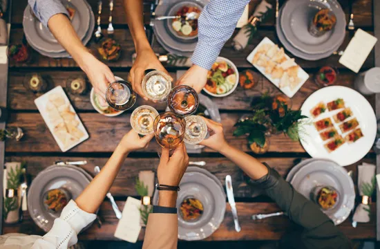 people toasting with various drinks over dining table filled with food and plates
