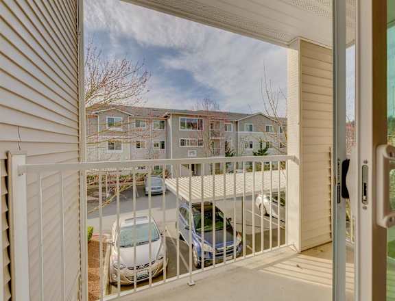 A view from a balcony looking out at a parking lot with cars and apartment buildings. at Valley Springs Apartments, Washington
