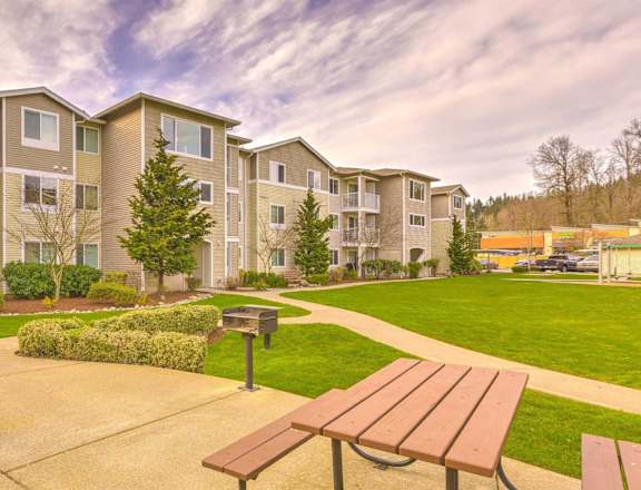Apartment complex with a grassy area and picnic tables in front. at Valley Springs Apartments, Washington