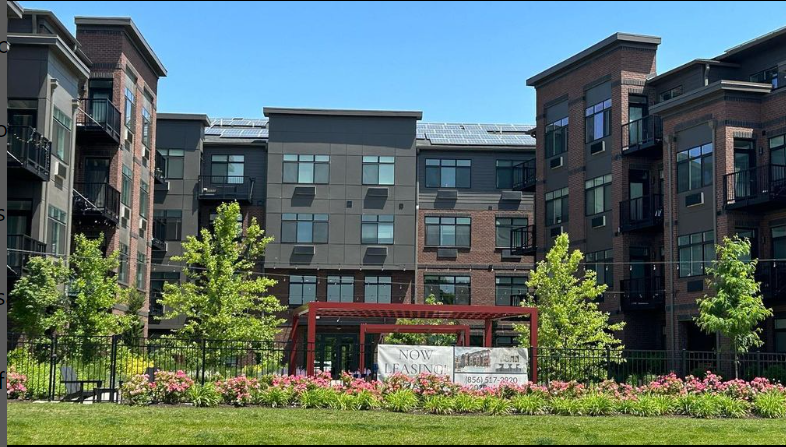 Modern apartment building with leasing sign and greenery.
