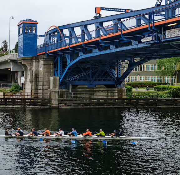 A group of people are rowing a boat under a blue bridge.