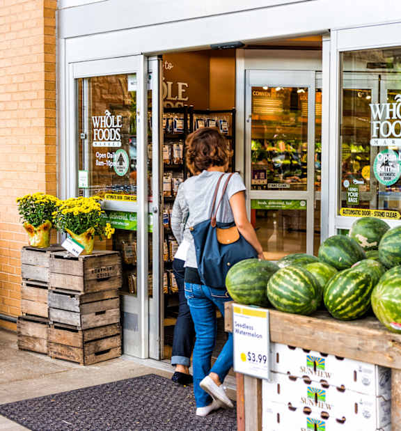 A woman is entering a Whole Foods store with a display of watermelons in front.