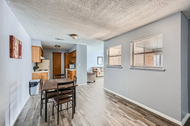 Dining area and kitchen in an apartment with light gray walls and wood-look flooring.