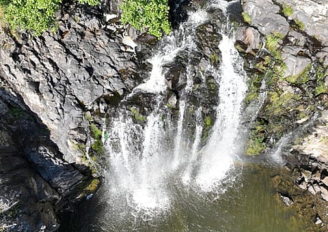 Breathtaking aerial view of a cascading waterfall surrounded by lush greenery and rugged rocks.