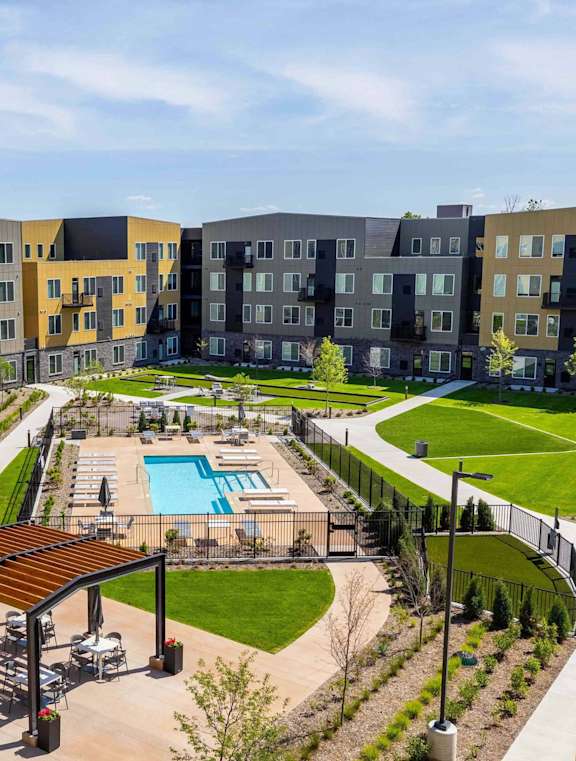 A large outdoor swimming pool is surrounded by a grassy area and a wooden pavilion.
