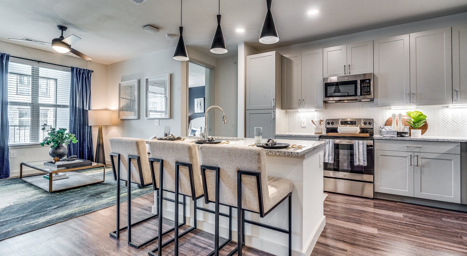 One-Bedroom Apartments in Grand Prairie, TX - Aven at the Cove - Modern Kitchen with Wood-Style Flooring, Stainless Steel Appliances, Granite Countertops, White Tile Backsplash, Grey Cabinets, and a Kitchen Island