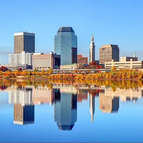 Vibrant city skyline and colorful autumn foliage reflected in a serene river, offering a breathtaking urban view.
