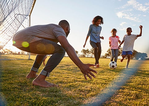 Joyful family playing soccer outdoors with children scoring a goal under the sunset, highlighting active lifestyle and bonding moments.