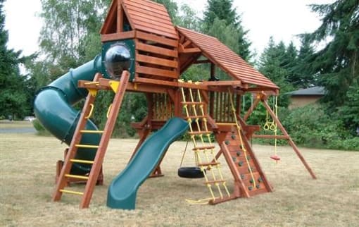 Dog-Friendly Apartments in Lacey, WA - Emerald Pointe - Playground With Wooden Jungle Gym, Green Spiral Tube Slide, Tire Swing, And Open Grassy Area.