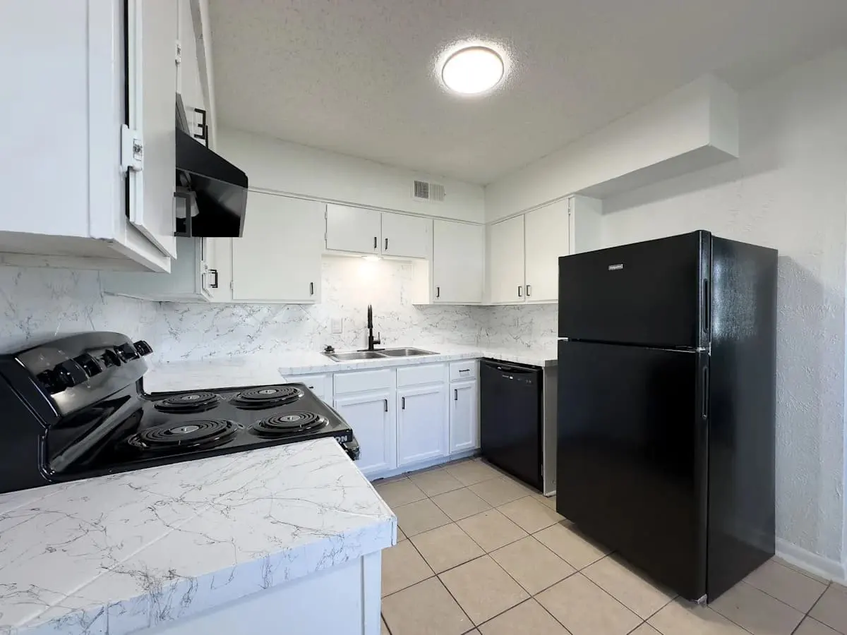 A modern kitchen featuring white cabinets, new countertops, and black appliances including a refrigerator and stove.