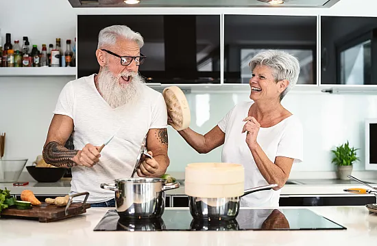 stylish elderly couple cooking in kitchen and laughing