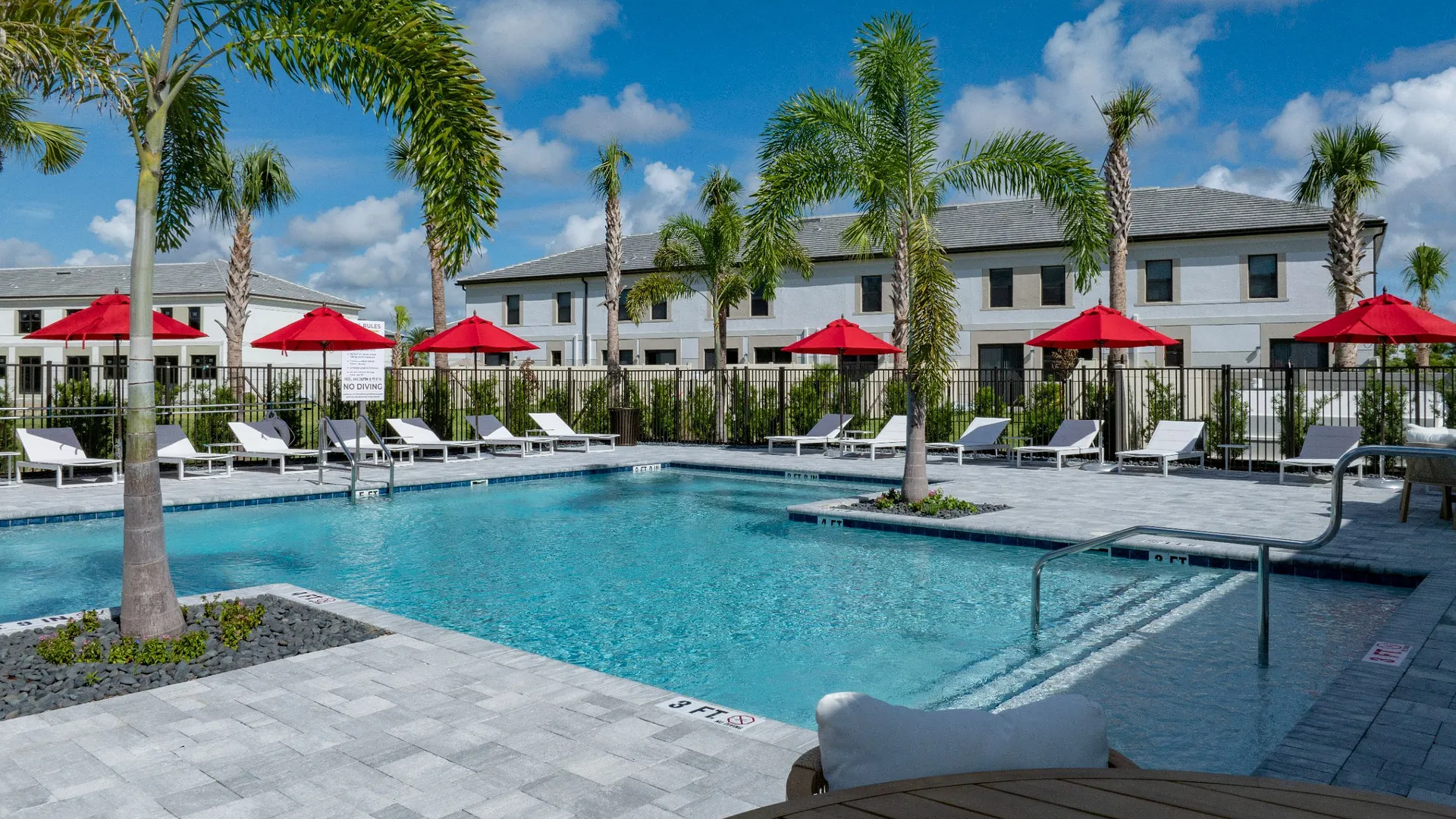 A sunny pool area surrounded by palm trees and red umbrellas.