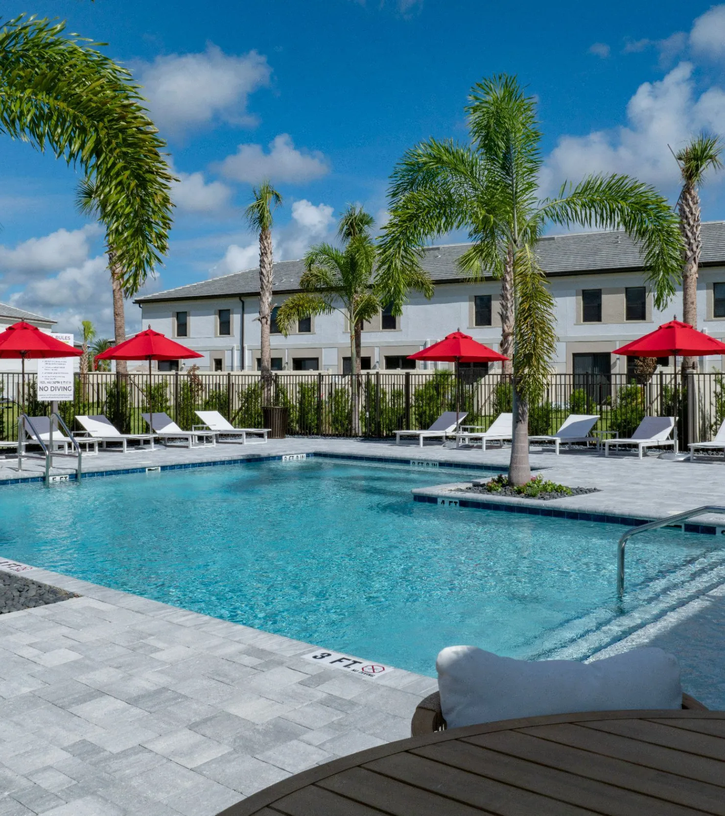 A sunny pool area surrounded by palm trees and red umbrellas.