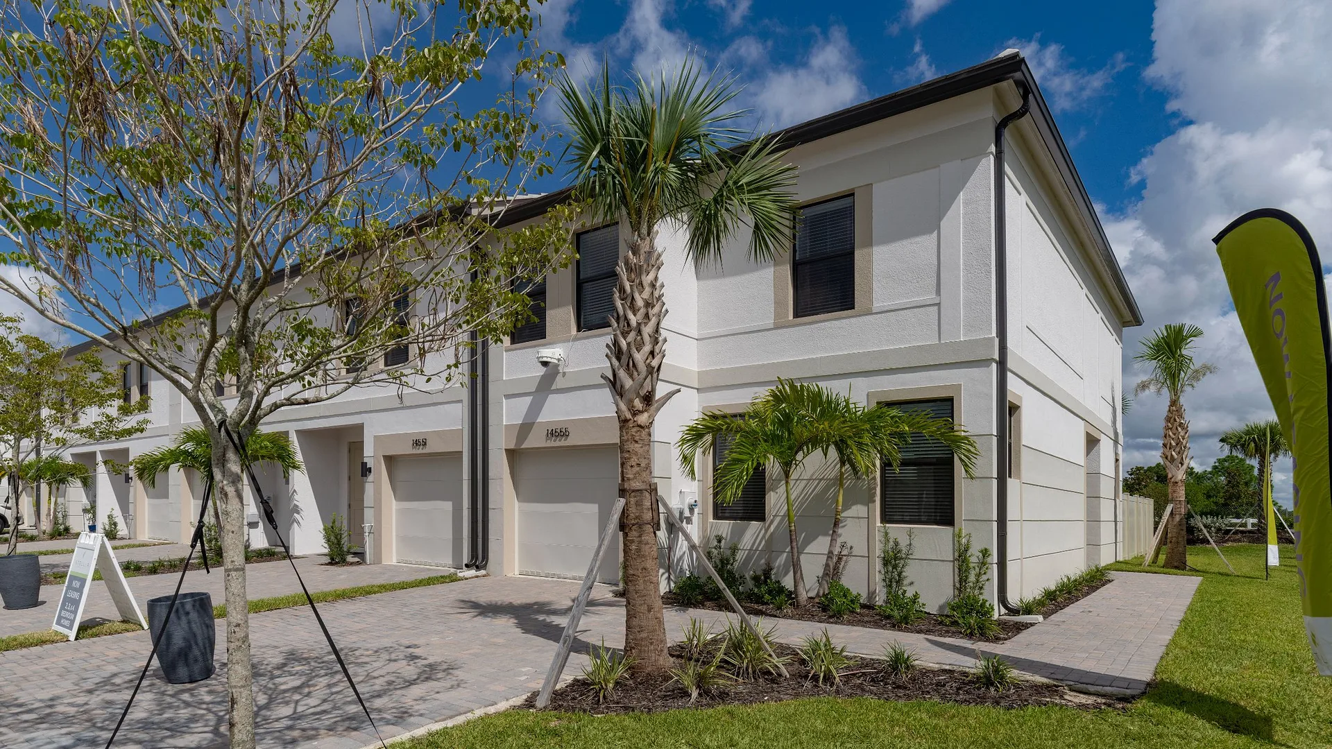 Newly constructed townhouses with palm trees and a paved driveway.