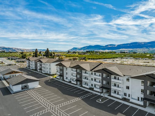 A parking lot in front of apartment buildings with a mountain range in the background.