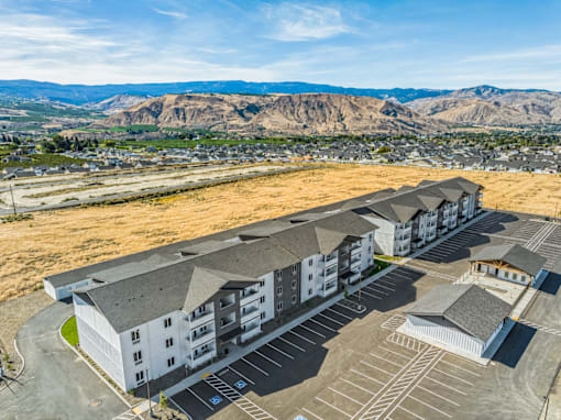 A large building complex with a parking lot in front and mountains in the background.