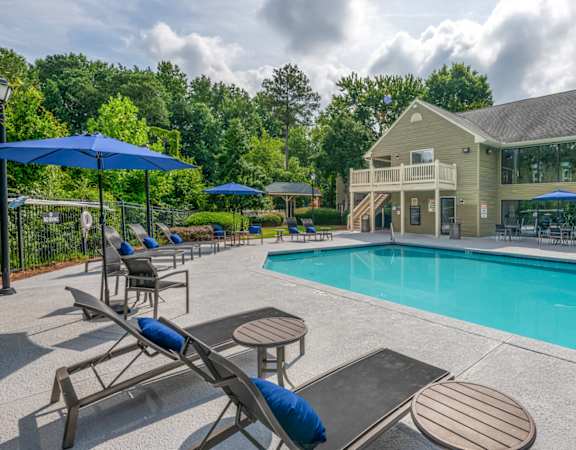 a swimming pool with chairs and umbrellas next to a house