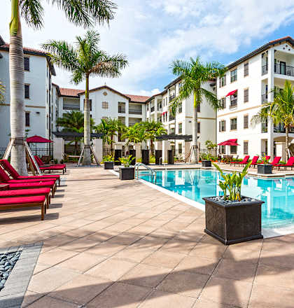 A pool surrounded by red chairs and palm trees.