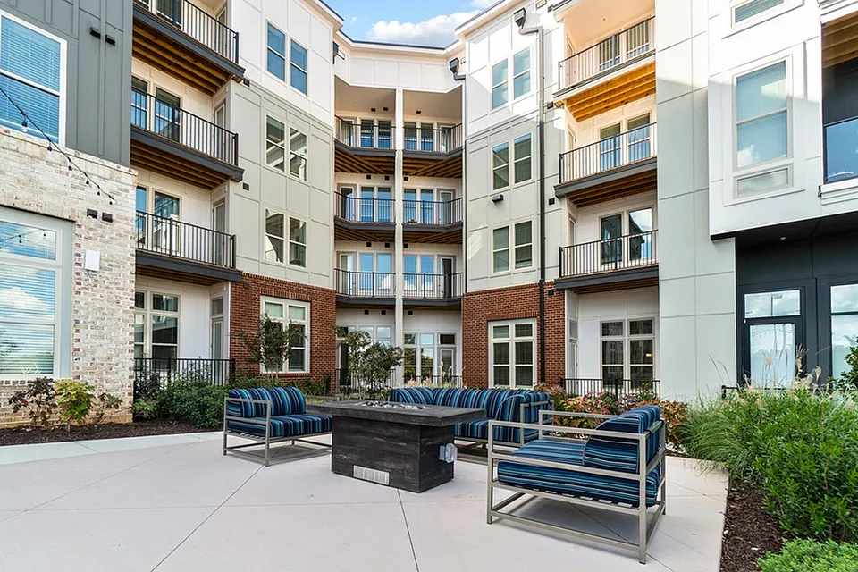 Contemporary apartment courtyard featuring stylish seating, lush greenery, and multi-story balconies.