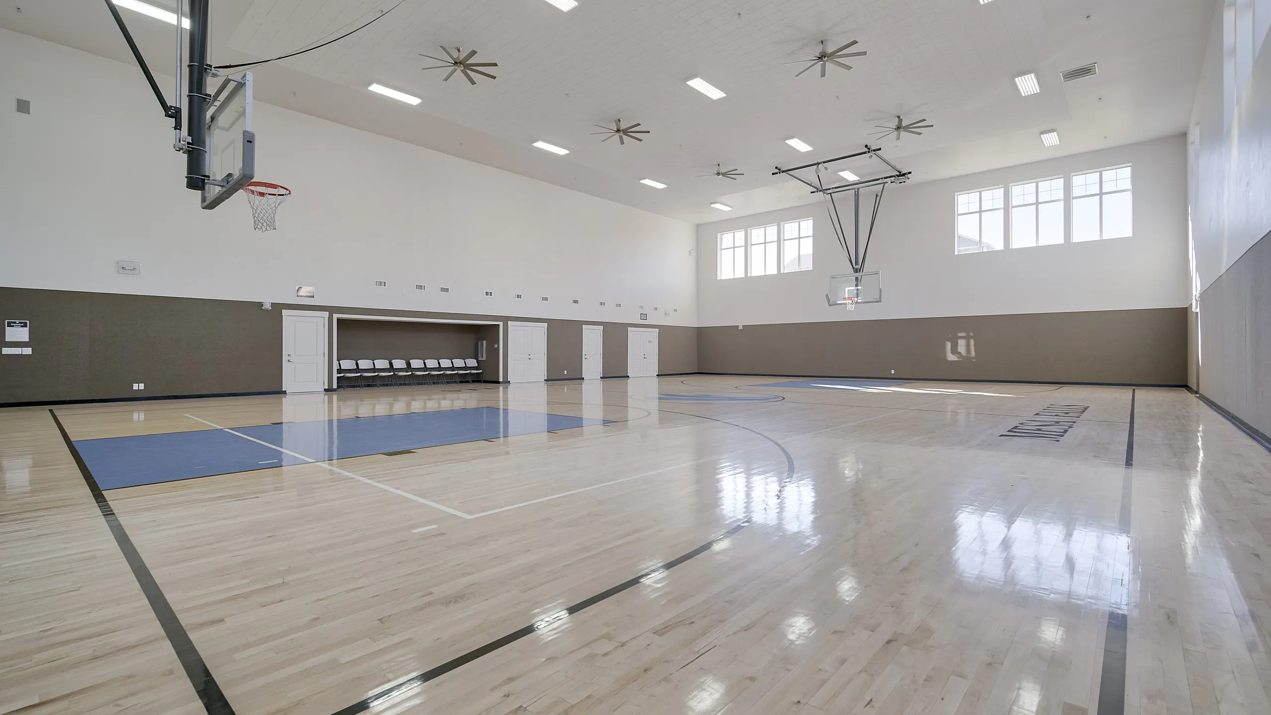 Spacious indoor basketball court with gleaming hardwood floors, high ceilings, and abundant natural lighting.