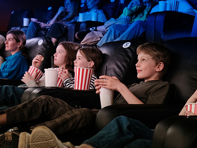 Families enjoying a vibrant cinema experience with popcorn and smiles, seated in comfortable recliner chairs.