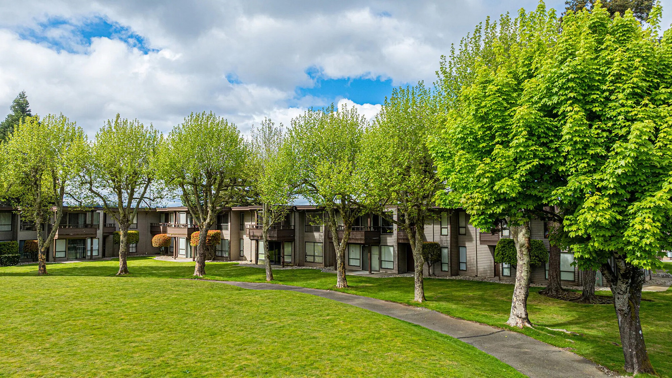 Charming apartment complex nestled amidst lush greenery with a spacious lawn and scenic paths.