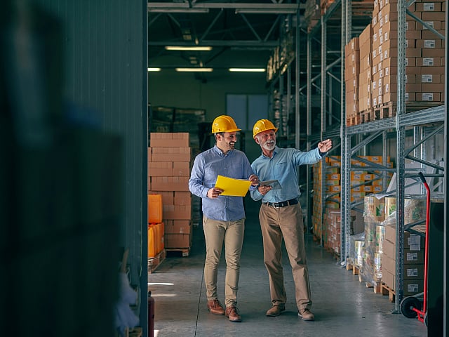 Professional warehouse team in hard hats reviewing plans amidst organized inventory, highlighting efficient storage solutions.