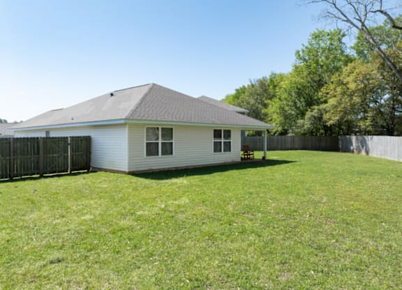 the backyard of a white house with a yard and a fence