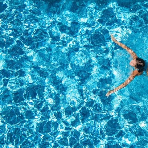 The Ensley 55+ Luxury Apartments with A person swims in a clear blue pool, seen from above, surrounded by sparkling water.