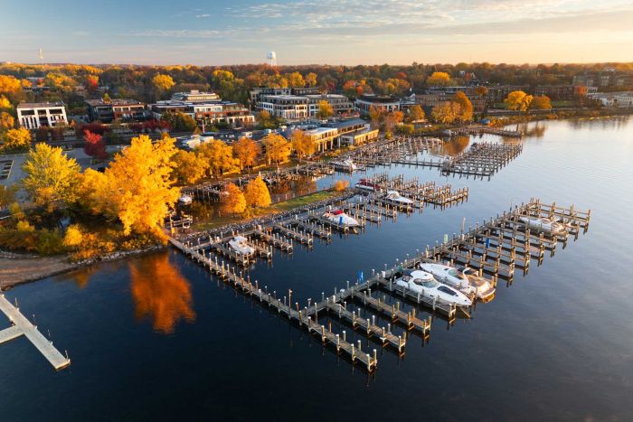 The Ensley 55+ Luxury Apartments with Aerial view of a marina with boats docked, surrounded by autumn trees and buildings near the shoreline.