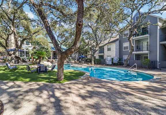 A swimming pool surrounded by trees and chairs in a sunny courtyard.