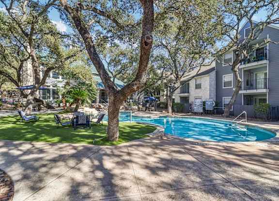 A swimming pool surrounded by trees and chairs in a sunny courtyard.