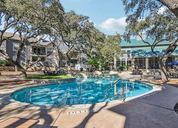 A swimming pool surrounded by trees and a building in the background.