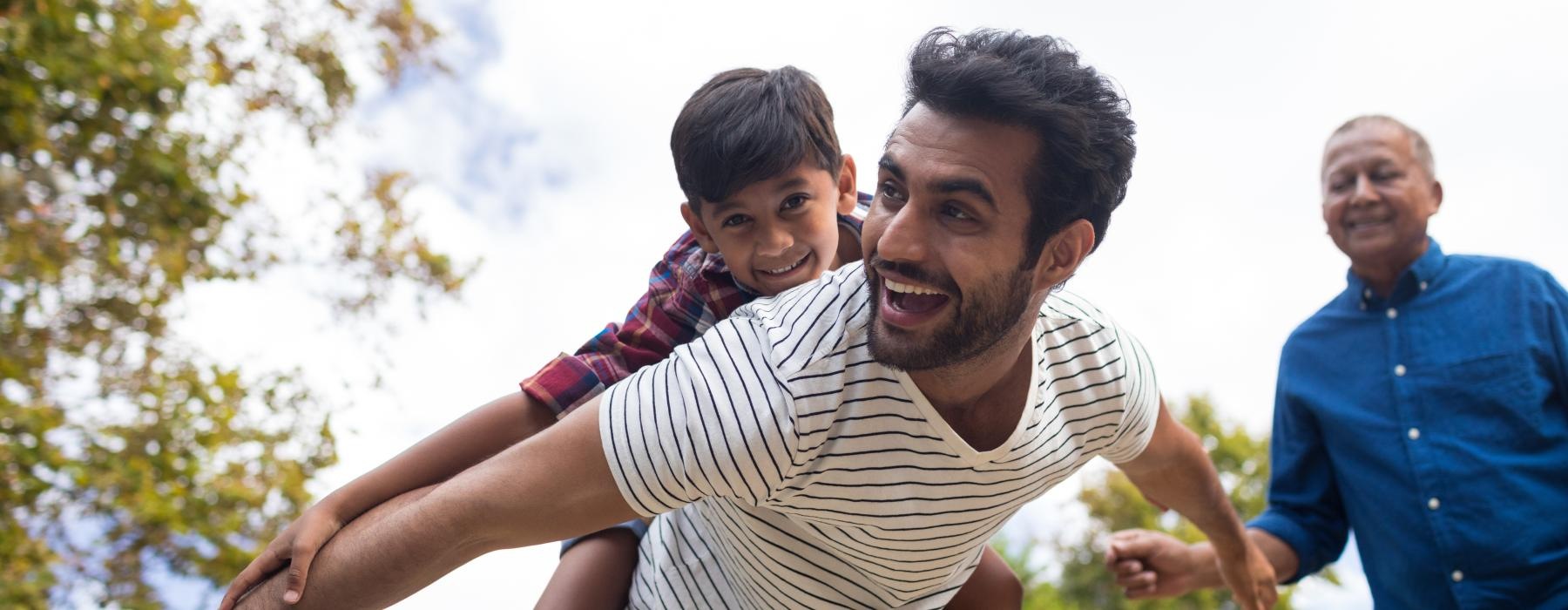 man plays in the park with a child on his back