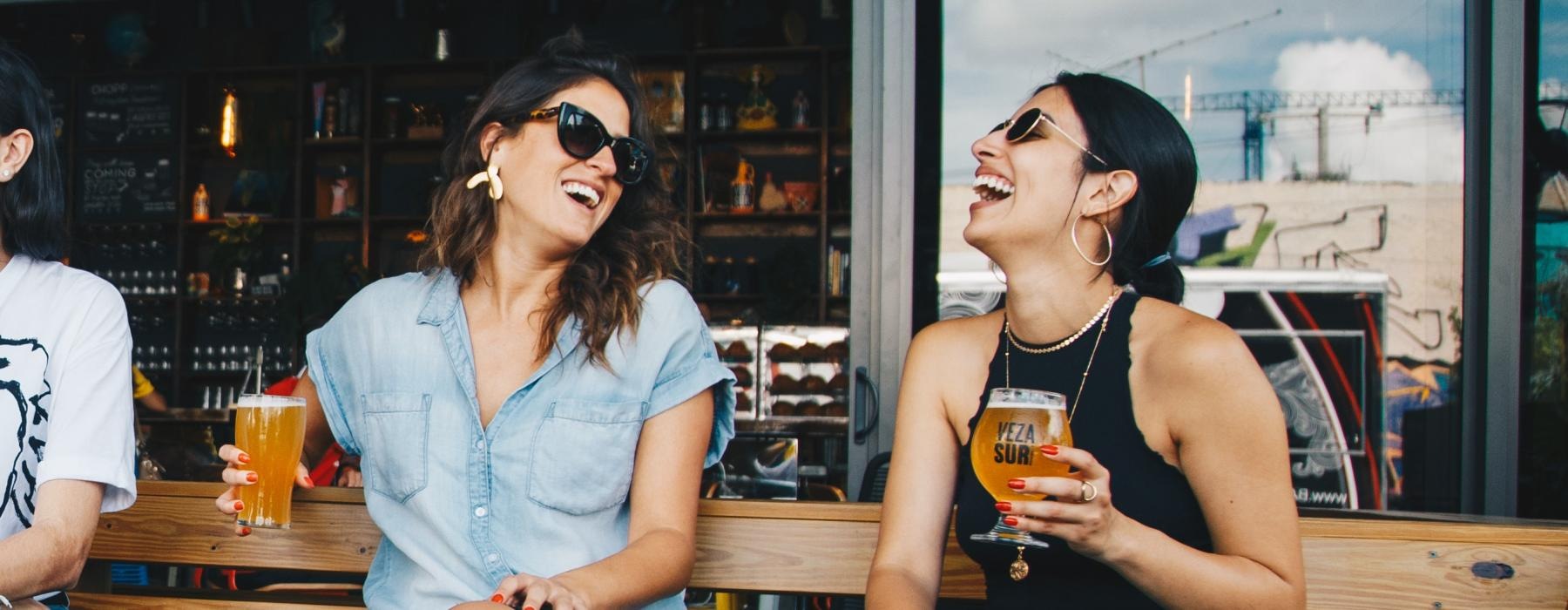 women sitting on a bench, with drinks in hand, outside a bar