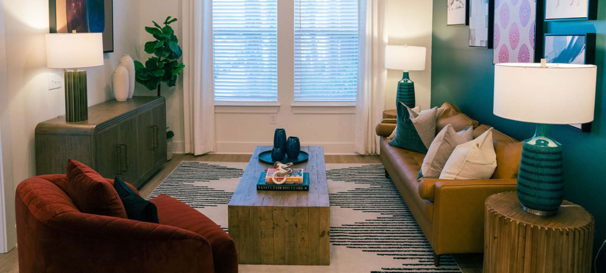 North Charleston, SC Luxury Apartments - Assembly at Park Circle - Living Room with Wood Plank Flooring, Area Rug, Sofa, Wooden Coffee Table, Side Tables with Lamps, Armchair, Storage Cabinet, and Large Window.