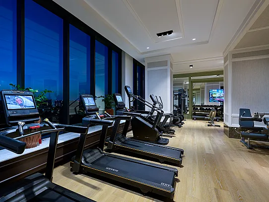 Modern fitness room with state-of-the-art treadmills and exercise equipment against a backdrop of large windows showcasing a stunning city view.